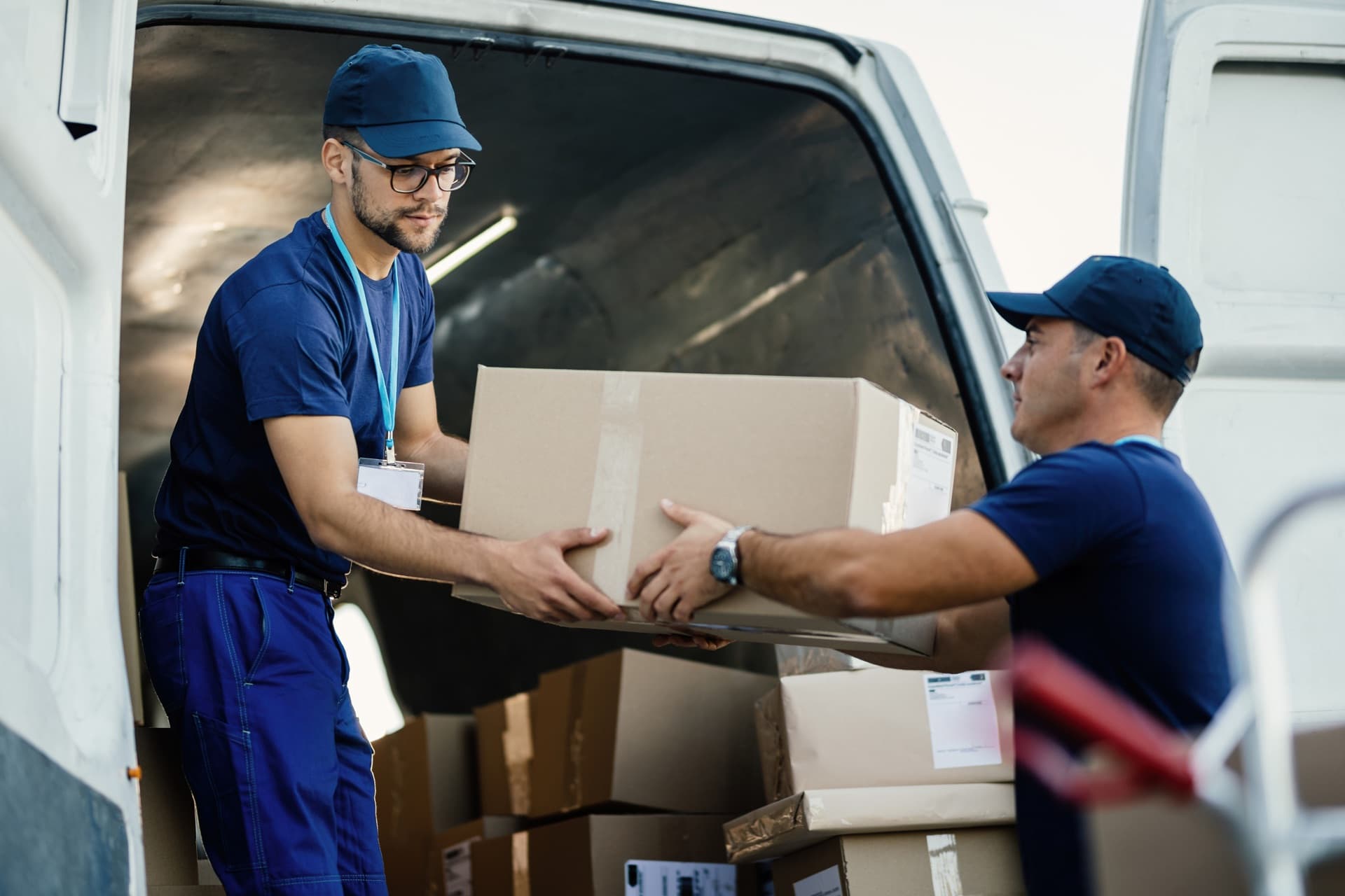 Two movers in uniform handing off a box at the back of a van